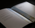 An open book or booklet photographed at an angle against a dark background, with blurred text on the pages and a soft light reflecting off the cover.