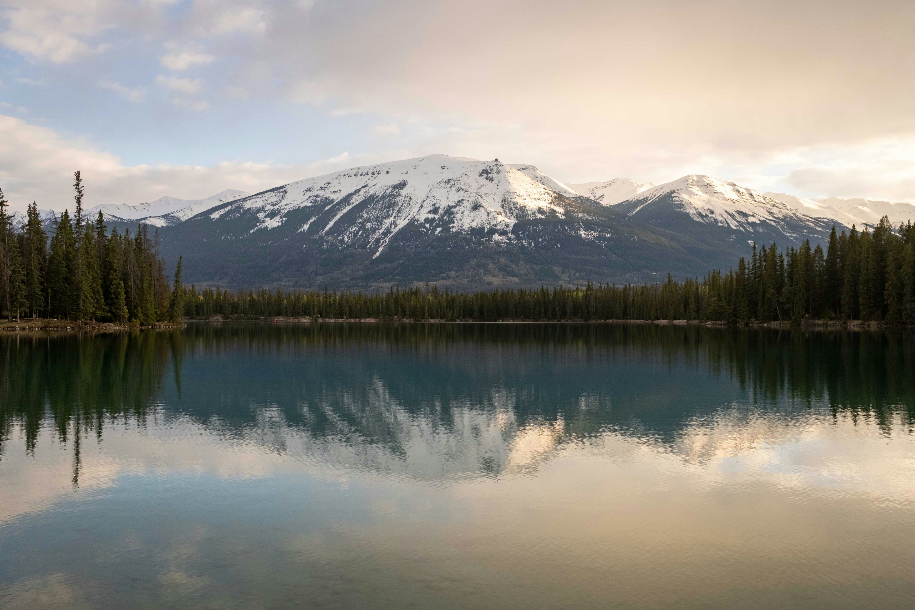 Calm mountain lake with snow-covered peaks and forest reflected in still water